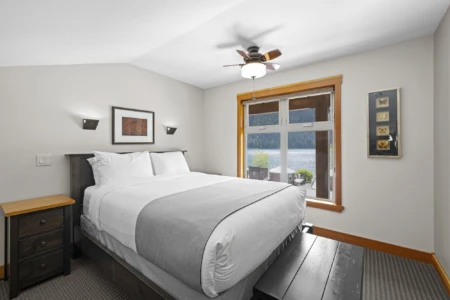 Moutcha Bay Lodge neatly arranged bedroom with a large bed, a ceiling fan, wall-mounted lights, artwork, and a view of the water through the window.
