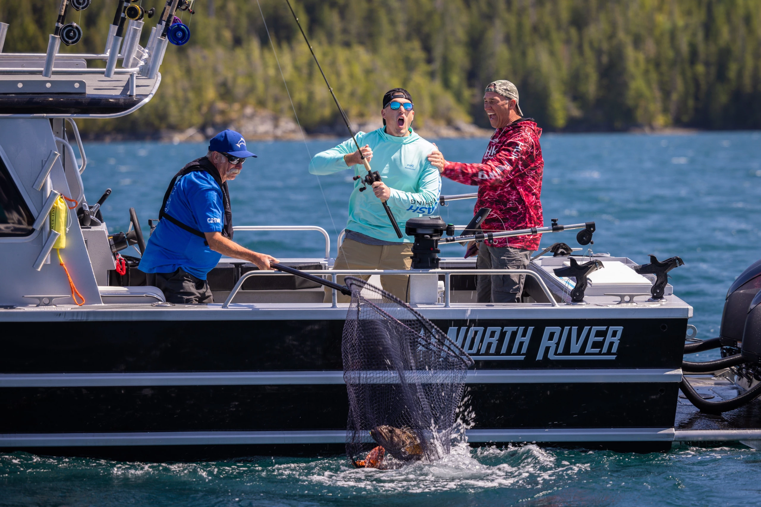 Two guest and a guide on a boat are engaged in fishing. The guide nets a large fish while one guest reels it in. They appear excited and focused.