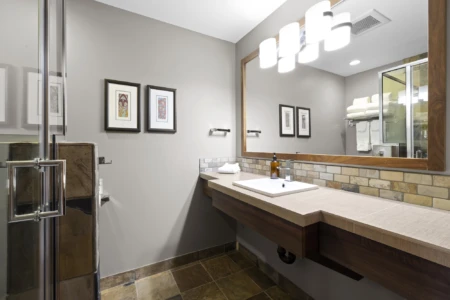Moutcha Bay Lodge bathroom with a floating vanity, rectangular sink, glass shower enclosure, tiled floor, and framed artwork on the walls.