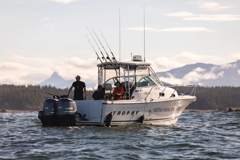 A Trophy fishing boat with guests on board floats in the water, surrounded by a scenic background with mountains and clouds in the distance.