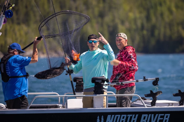 Three guest are on a boat, excitedly catching a fish with a net. They wear sunglasses and casual fishing gear, surrounded by fishing equipment.
